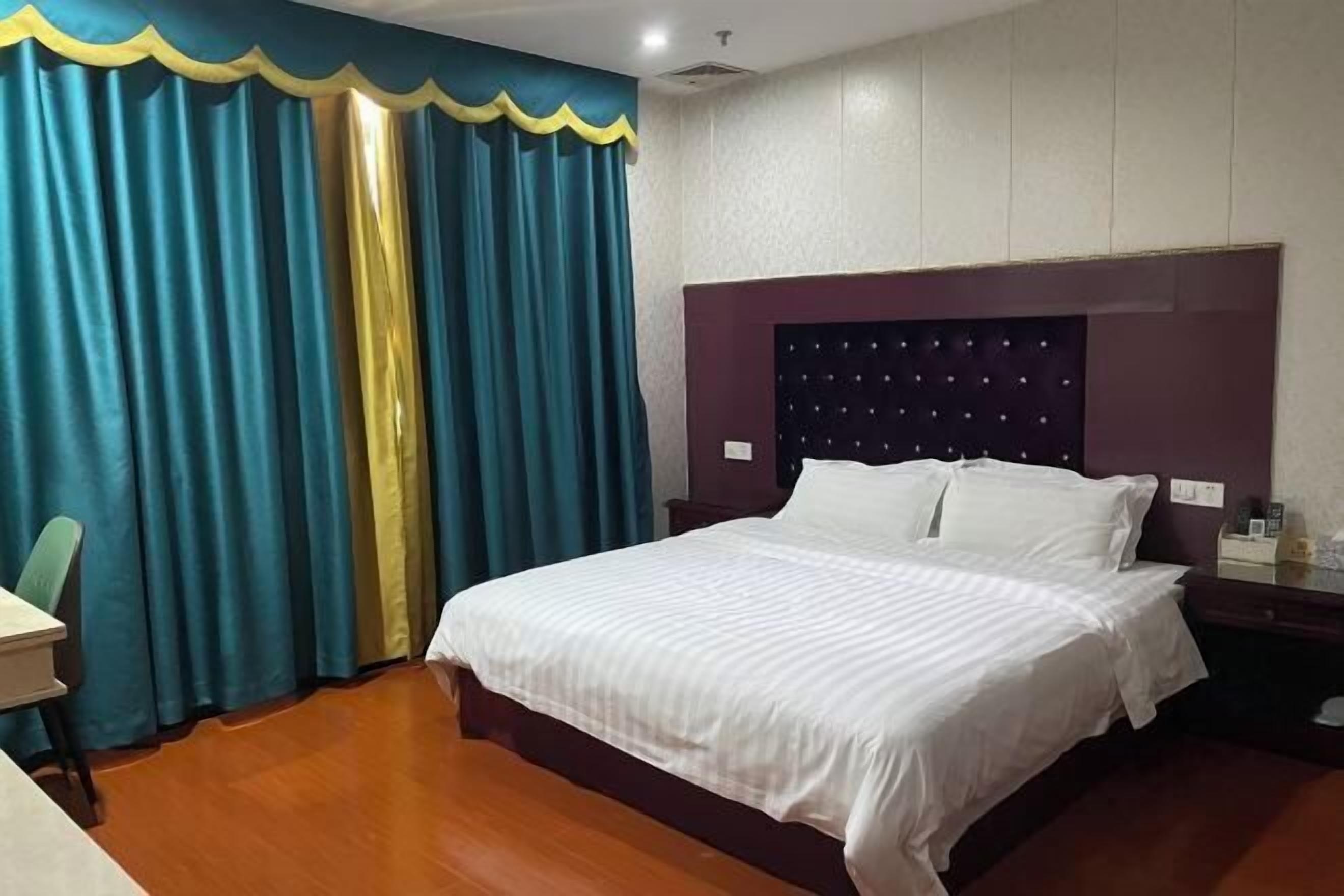 A hotel room with a large bed, a nightstand, a desk, and a chair.