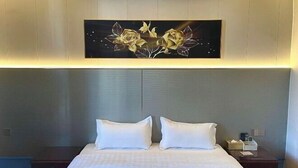 A hotel room with a large bed, two pillows, a nightstand with a lamp, and a wall-mounted artwork of flowers. - Zhaoqing Dengfeng Business Hotel B (Huaiji)