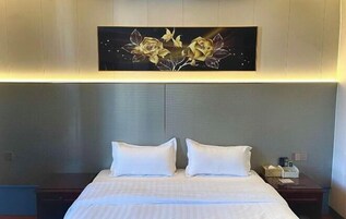 A hotel room with a large bed, two pillows, a nightstand with a lamp, and a wall-mounted artwork of flowers.
