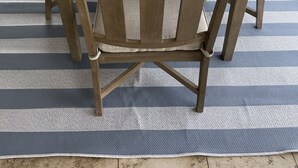 Ein Holztisch mit Stühlen und einem Blumentopf auf einer blau-weißen Streifenmatte.
