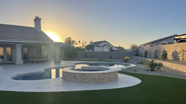 Ein angelegter Garten mit einem runden Steinbrunnen, einem Schwimmbad und einem Haus im Hintergrund.