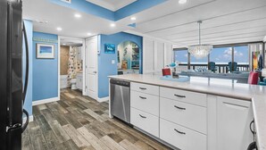 A modern kitchen with white cabinets, a stainless steel dishwasher, and a blue accent wall.