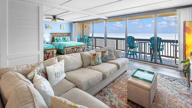 A spacious living room with a large sofa, a coffee table, and a view of the ocean through large windows.