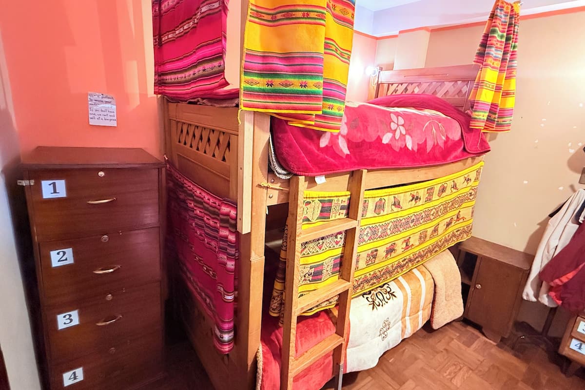 Ein Stockbett mit bunten Decken, eine Holzkommode mit Schubladen und ein kleiner Schrank mit nummerierten Schubladen.