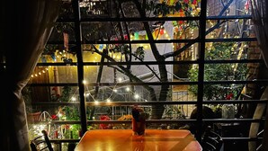 A dining area with a table and chairs, a window with a view of indoor plants and decorations, and a curtain partially covering the window. - Casa de huespedes La Casa Bonita (La Paz)