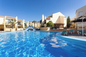 A swimming pool with a blue staircase leading to a building, surrounded by buildings with balconies and a palm tree. - Home2Book Dream Apartment Blue Coast Sun Fañabé (Adeje)