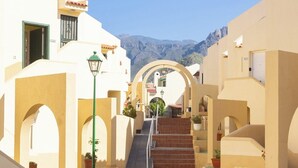 Une rue étroite bordée de bâtiments blancs, un escalier et une montagne en arrière-plan.