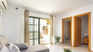 Un salon moderne avec un canapé, une table basse et une vue sur l’extérieur, accessible par une porte vitrée.