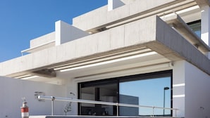 Un edificio moderno con techo plano, ventanas amplias y un balcón con barandilla de metal.