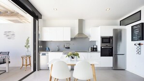 Una cocina moderna con armarios blancos, electrodomésticos de acero inoxidable y un comedor con sillas blancas.