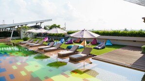 Un espace piscine aménagé sur le toit, avec des chaises longues et des parasols, entouré de verdure et surplombant un ciel dégagé.