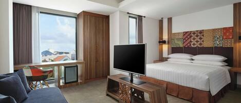 A modern hotel room with a large bed, a TV, a desk, and a view of the city.