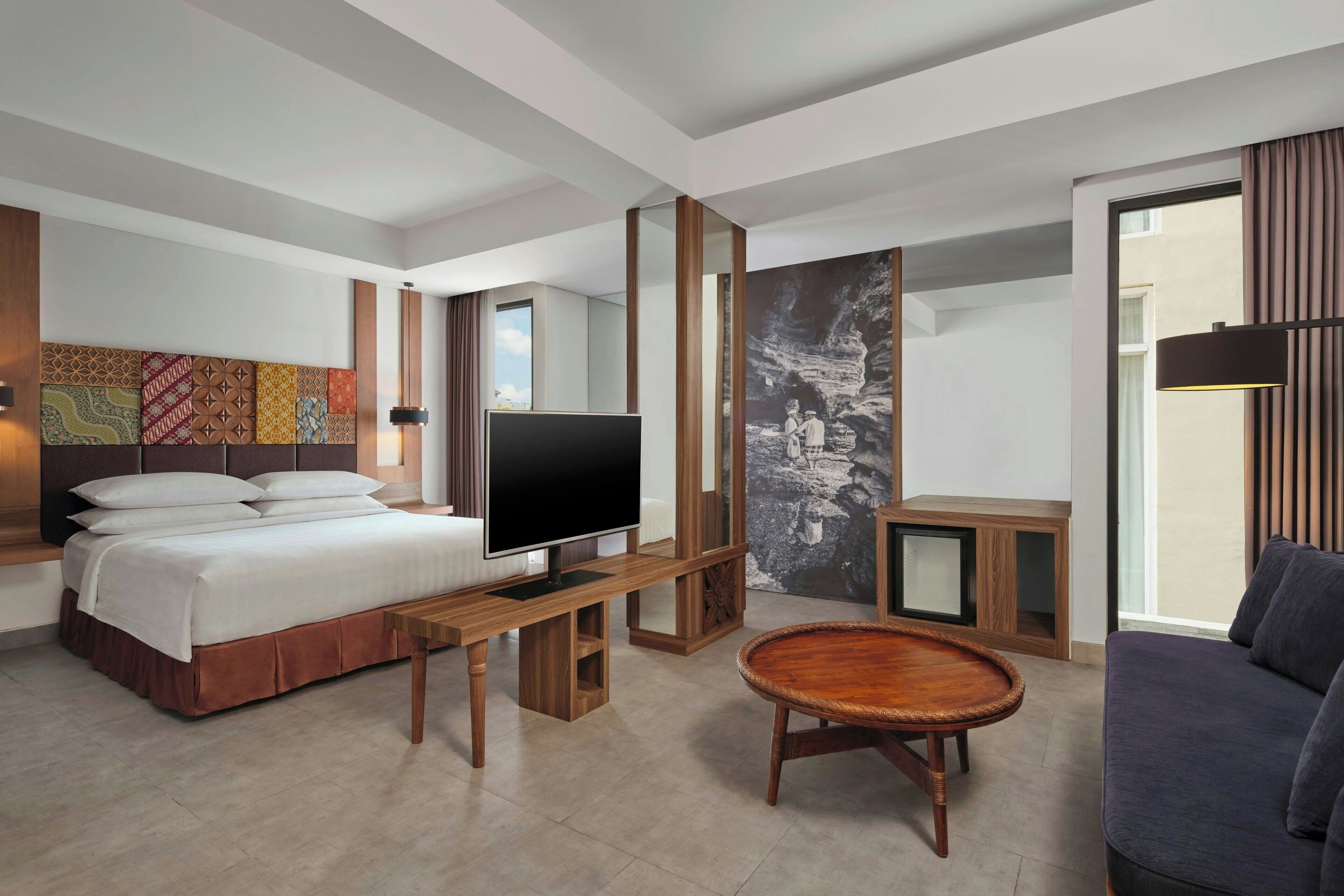 A modern hotel room with a bed, TV, wooden furniture, and artwork on the walls.
