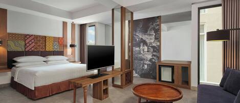 A modern hotel room with a bed, TV, wooden furniture, and artwork on the walls.