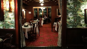 Ein Restaurant mit Holztischen und -stühlen, einem roten Teppichboden und Blick ins Freie durch große Fenster.