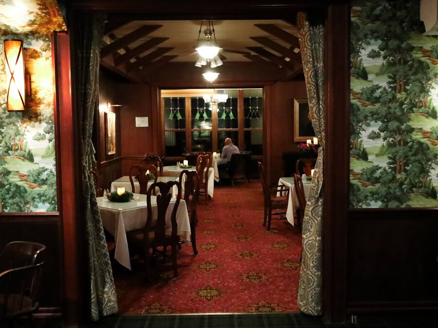 A restaurant with wooden tables and chairs, a red carpeted floor, and a view of the outdoors through large windows.
