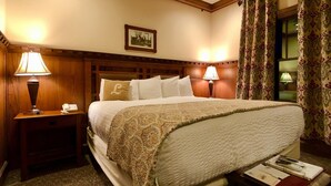 Ein Hotelzimmer mit einem großen Bett, zwei Nachttischlampen, einem Holz-Kopfteil, einem gerahmten Bild an der Wand und einem Fenster mit Vorhängen.