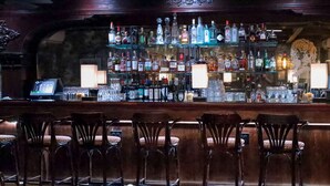 Eine Barbereich mit zahlreichen Spirituosenflaschen, Gläsern und einer Bar. Vor der Bar stehen mehrere Stühle.