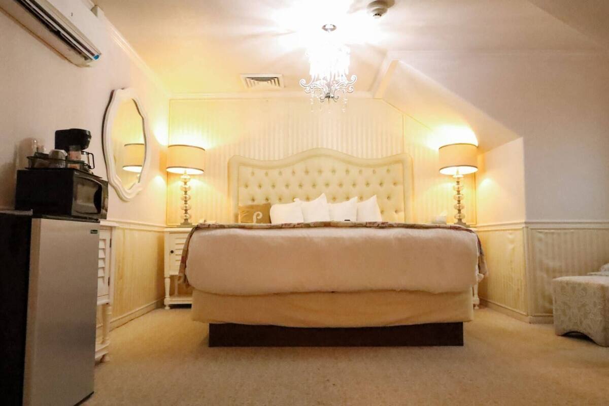 A hotel room with a large bed, two bedside lamps, a chandelier, and a small table with a lamp.