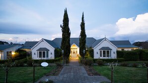 Ein zweistöckiges Haus mit einem zentralen Eingang, das von zwei hohen Bäumen gesäumt wird, und einem gepflegten Garten.