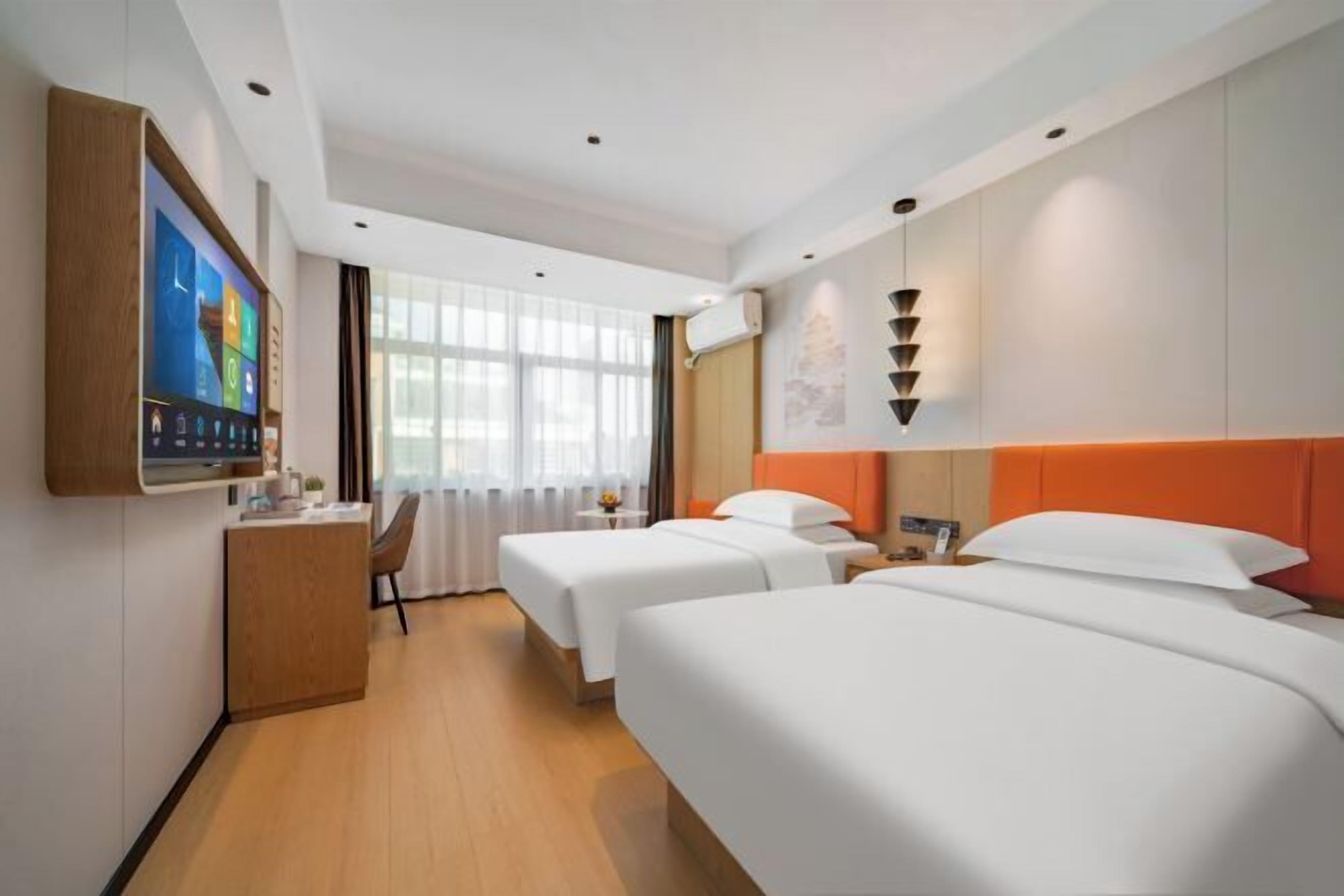 Una habitación de hotel con dos camas, un escritorio, un televisor y una ventana con cortinas.