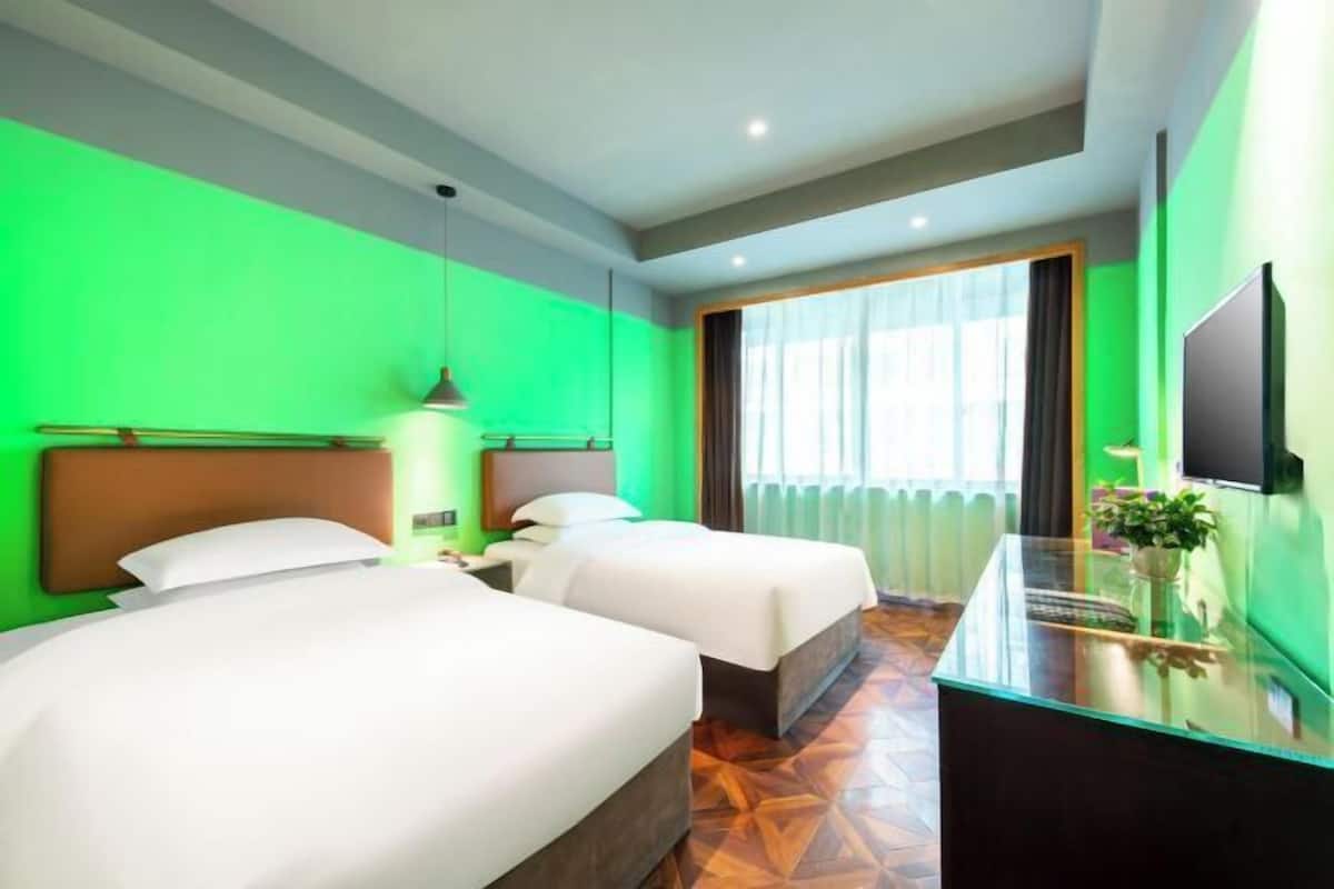 A hotel room with two beds, a glass desk, a television, and a large window with curtains.