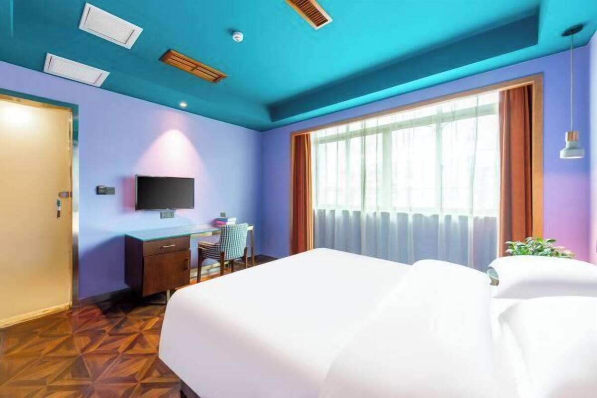 A hotel room with a bed, a desk, a chair, a TV, and a window with curtains.