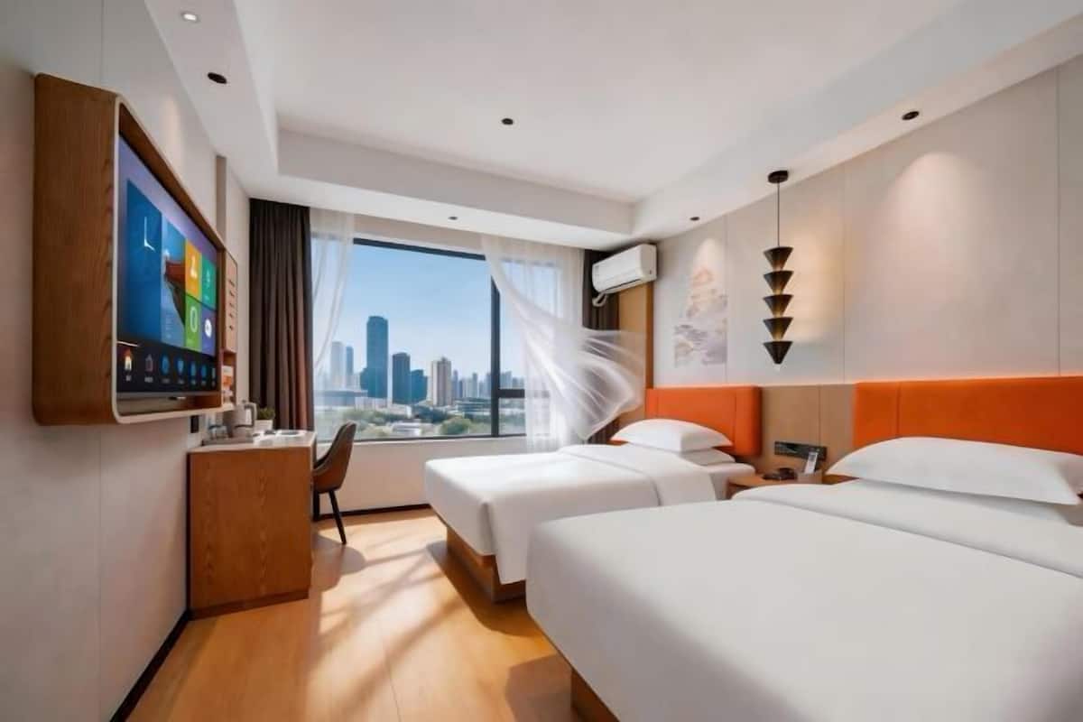 A hotel room with two beds, a desk, a TV, and a city view.