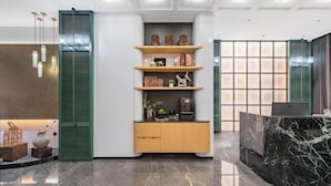 Un área de recepción moderna con un mostrador de mármol, un mueble de madera con adornos y una pared verde con estantes que exhiben libros y objetos decorativos.