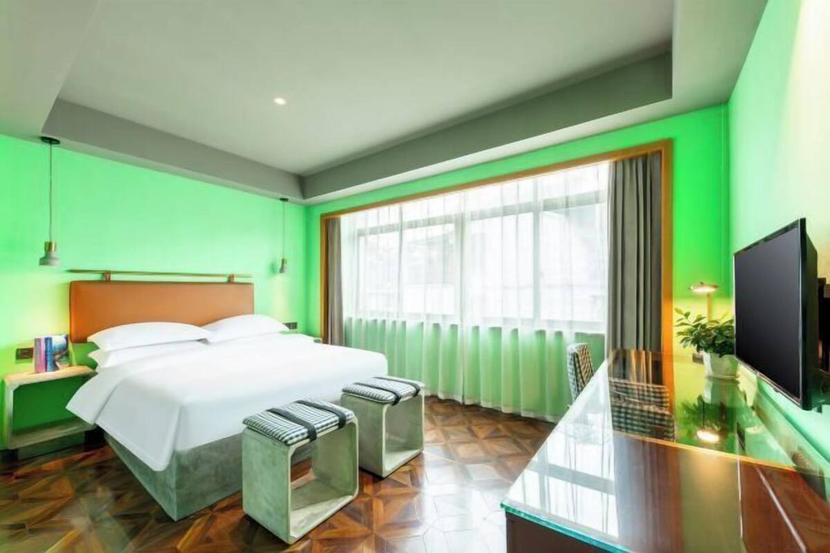 A hotel room with a bed, bedside tables, a TV, and a large window with curtains.