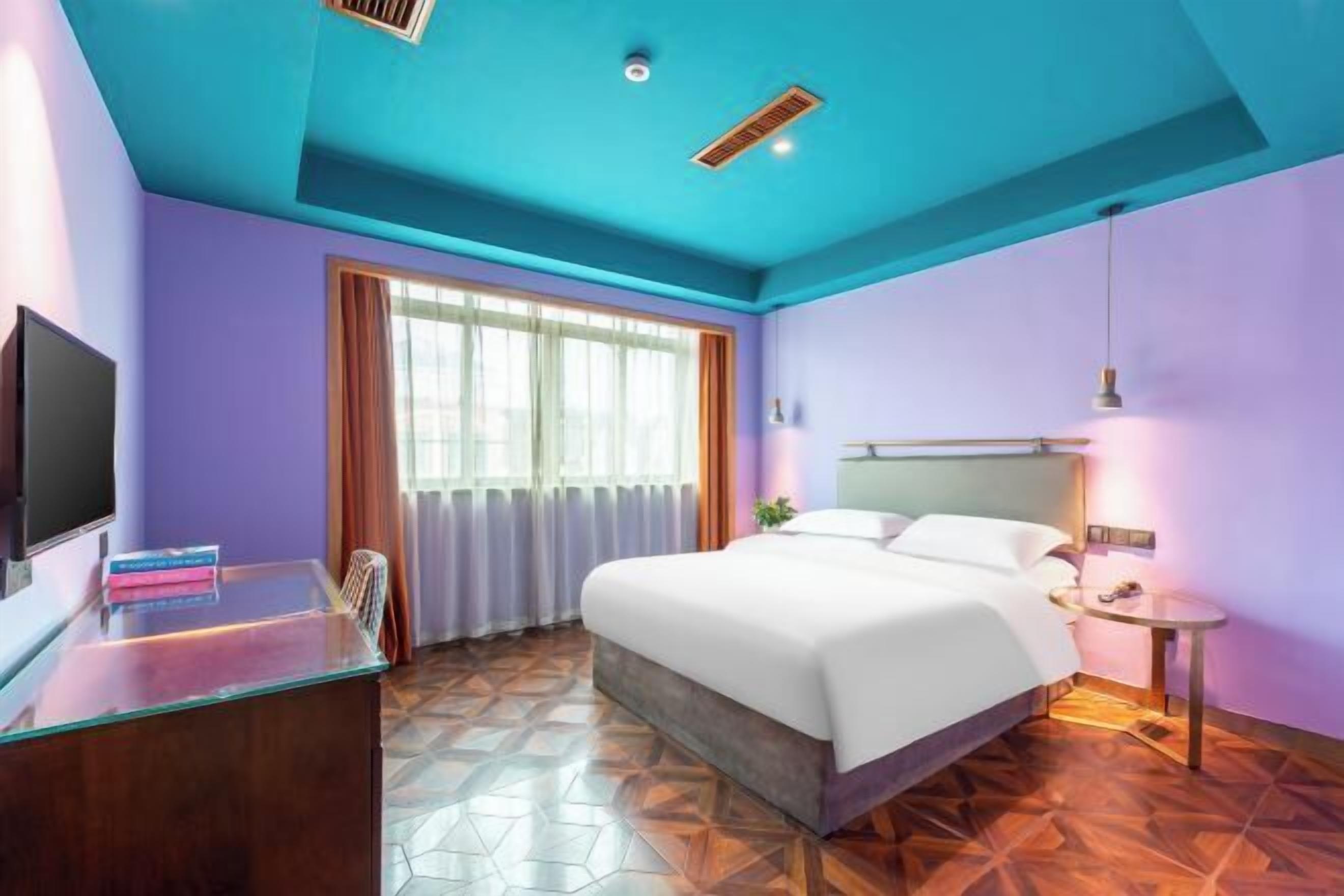 Une chambre d’hôtel avec un lit, un bureau, une télévision et une fenêtre avec des rideaux.