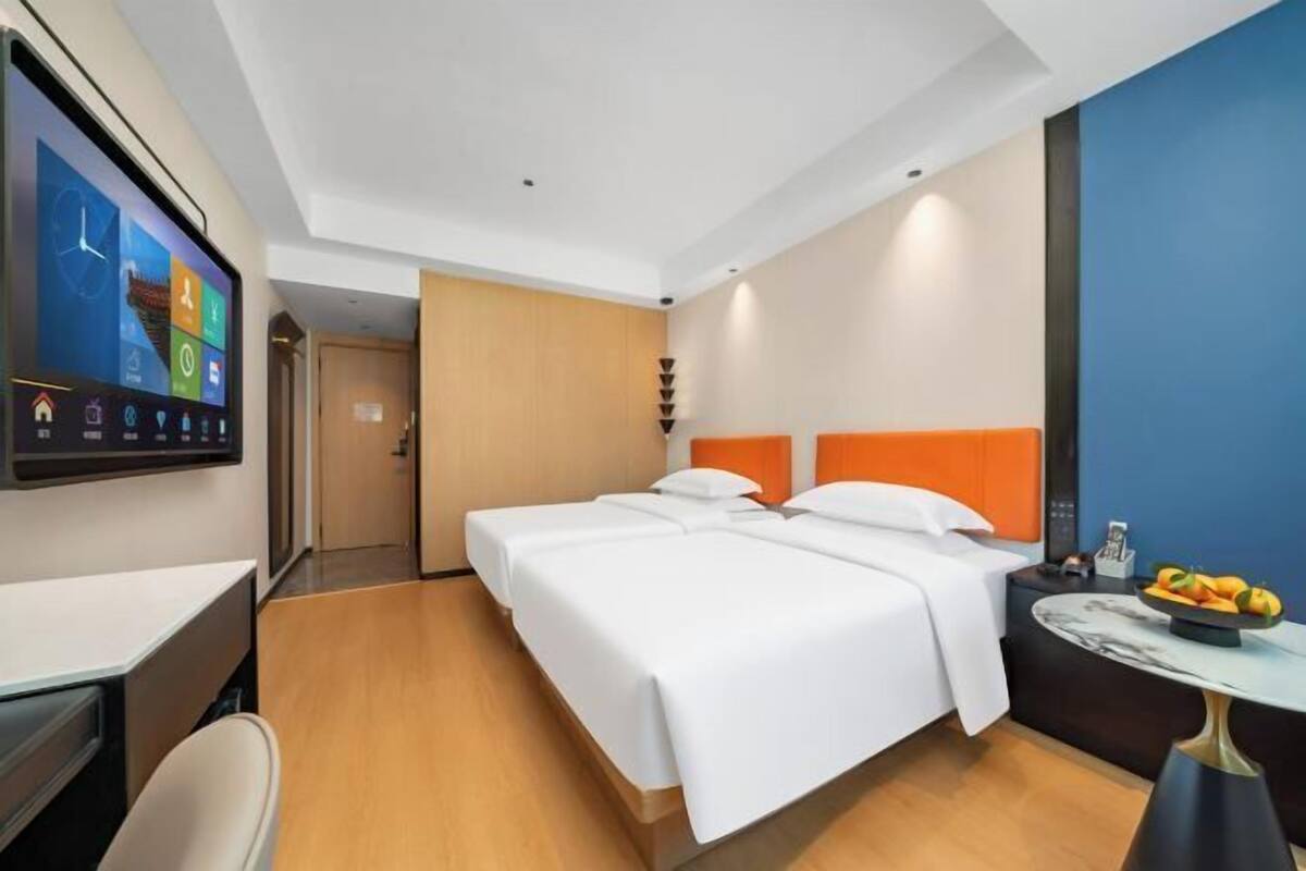A hotel room with a large bed, a desk, and a TV displaying a weather app.