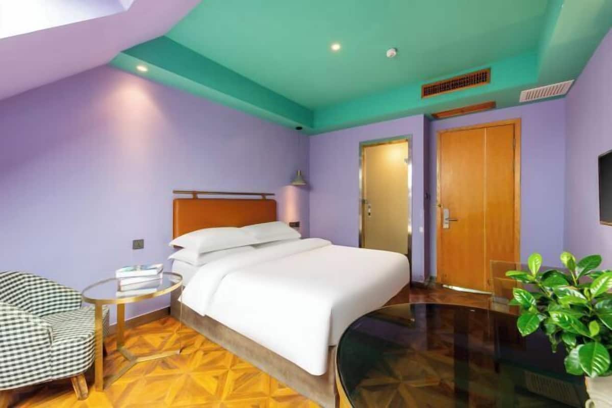 A bedroom with a bed, a chair, a small table, and a plant.