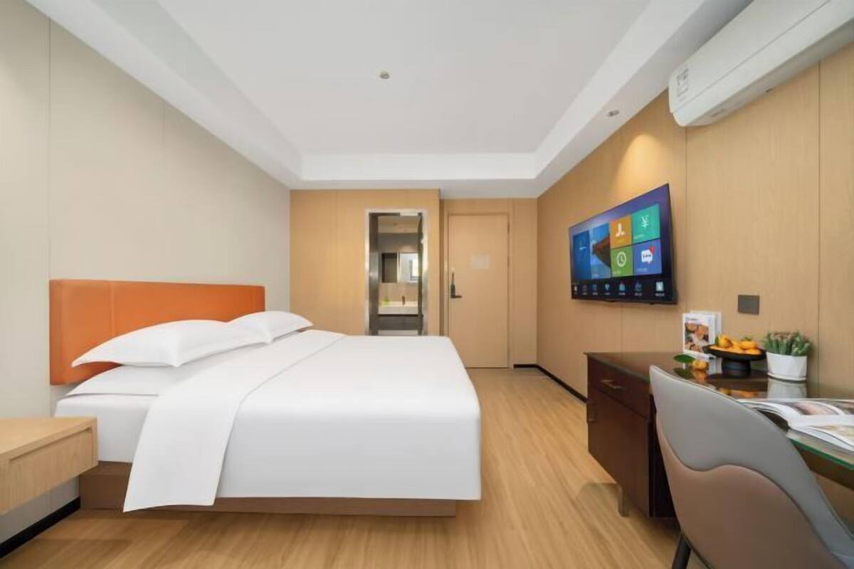 A hotel room with a bed, a desk, a chair, and a television displaying a Windows interface.