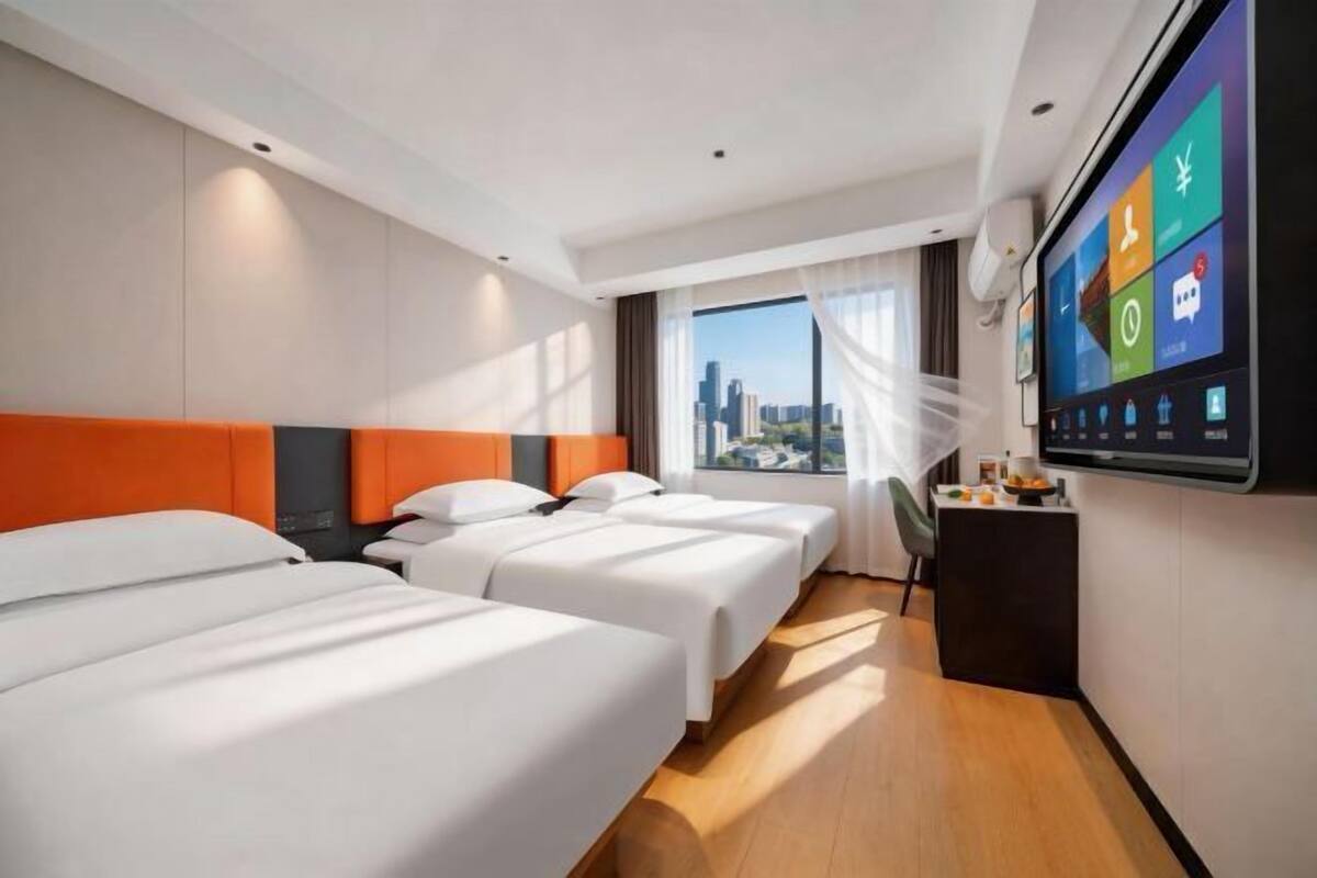 A hotel room with two beds, a desk, a TV, and a city view.