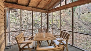 Un belvédère en bois avec une table et des chaises, de grandes fenêtres et une vue sur une zone boisée.
