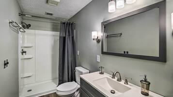 A modern bathroom with a glass shower enclosure, a toilet, a sink with a mirror, and a shower curtain.