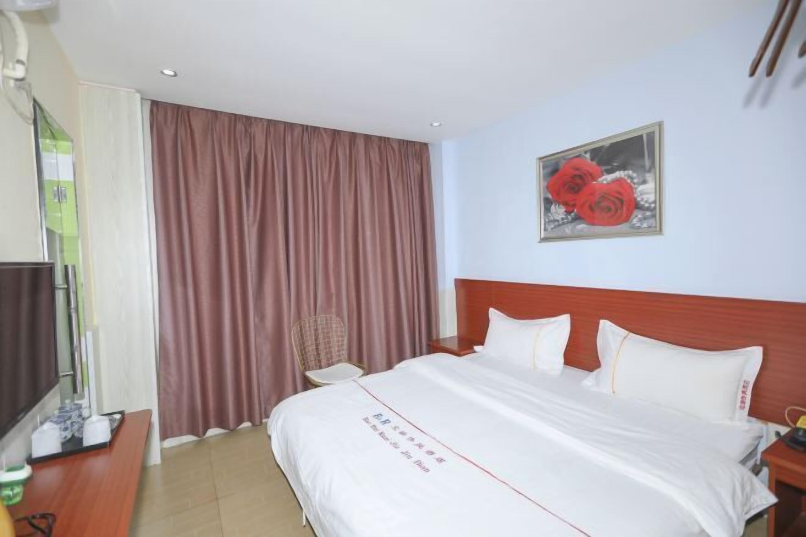 Hotellihuone, jossa on sänky, televisio, tuoli ja seinällä punakukkia kuvaava taulu.