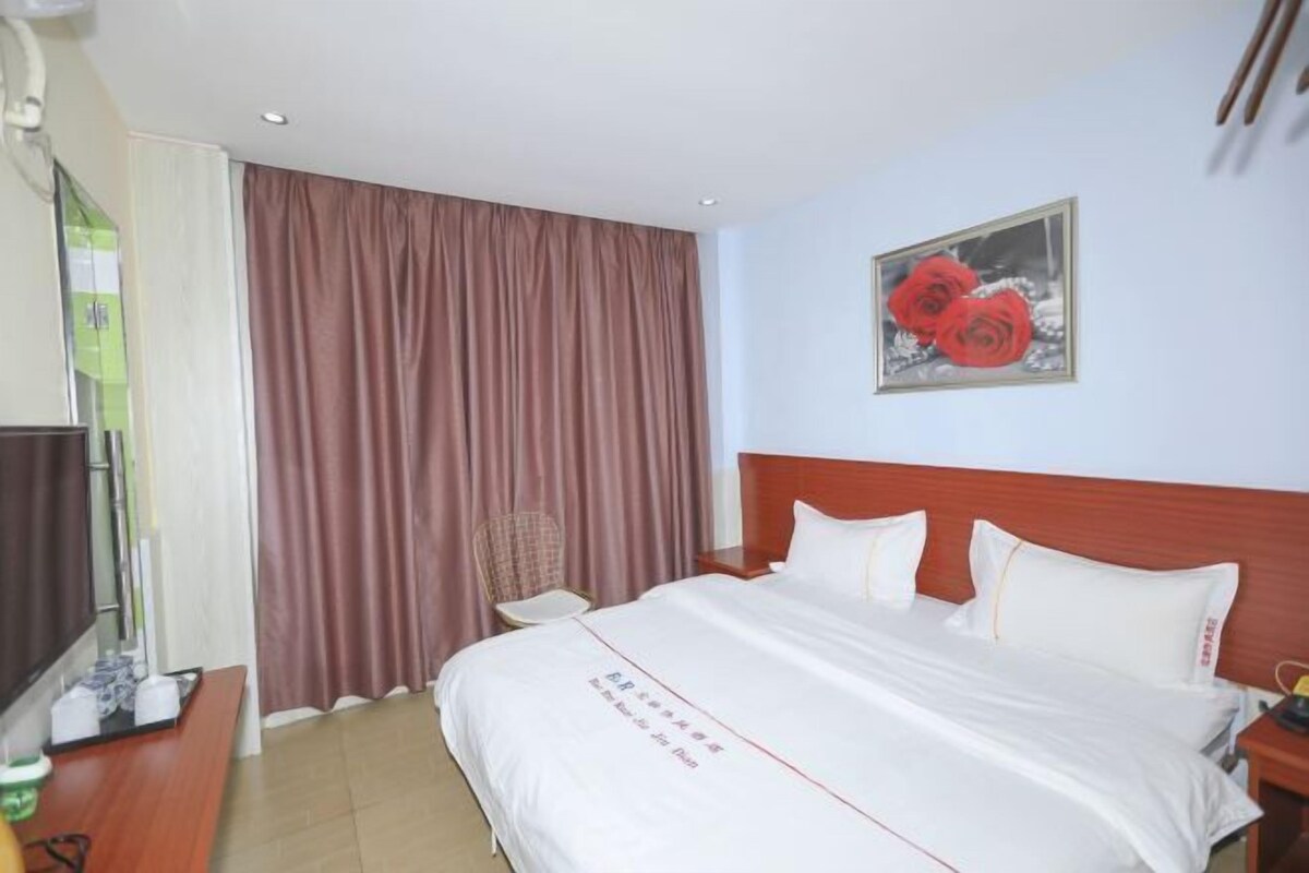 Habitación de hotel con cama, televisión, una silla y un cuadro de flores rojas en la pared.