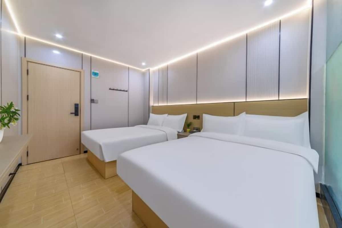 A hotel room with two beds, a bedside table, a nightstand, a potted plant, and a door.