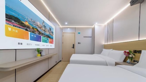 Camera d'albergo con due letti, un comodino con un vaso di fiori, una TV a parete e un quadro.
