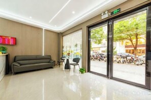 A hotel lobby with a reception desk, a sofa, a small table, and a large window with a view of the street. - Baorui Hotel (Shenzhen Bao'an International Airport T3 Terminal Hourui Subway Station) (Shenzhen)