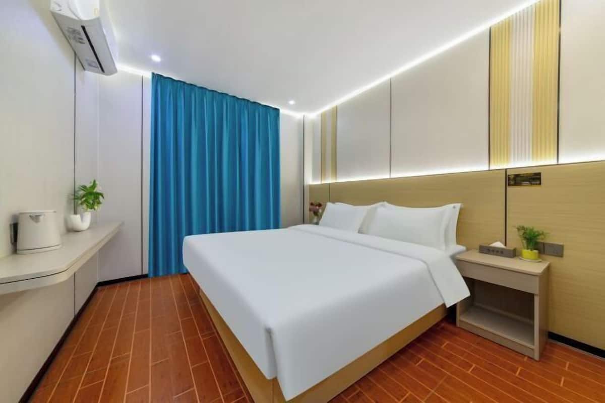 A hotel room with a bed, a nightstand, a wall-mounted air conditioner, and a blue curtain.