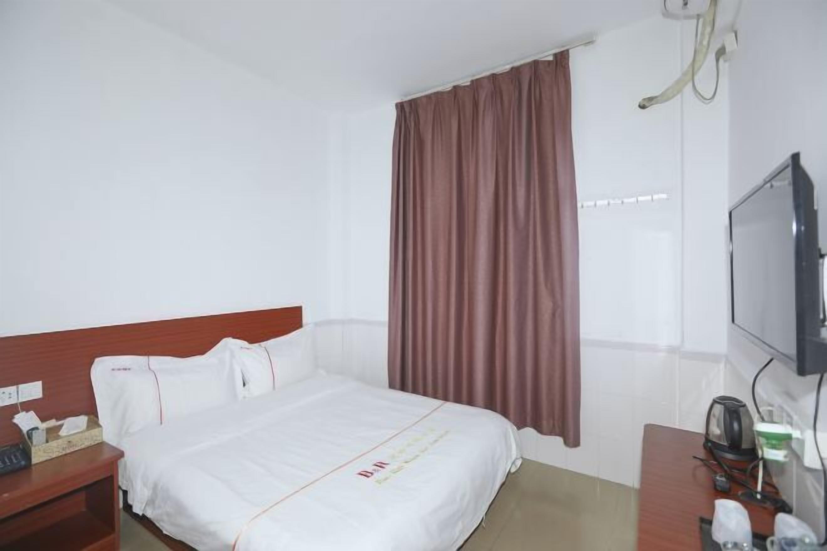 Une chambre d’hôtel avec un lit, un bureau avec un ordinateur, une télévision et une fenêtre avec des rideaux.