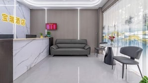 Una moderna area reception di un hotel, con una scrivania in marmo, un divano grigio e un tavolino con sedie.