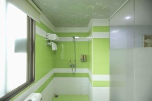 Un baño pequeño, bien iluminado, con azulejos verdes y blancos, una ducha y una ventana.