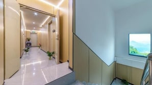 Una hall d'hotel moderna con pavimento in marmo, una scala e vista su spazi verdi attraverso una finestra.