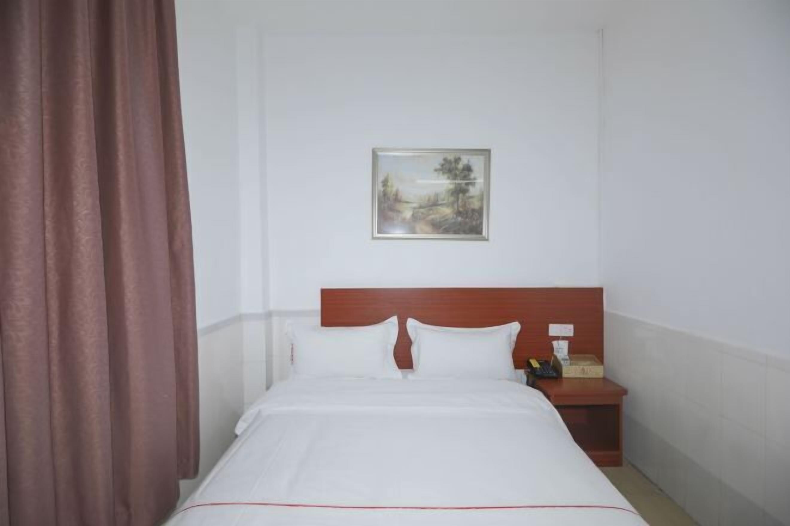 A hotel room with a bed, a nightstand, a painting on the wall, and a brown curtain.