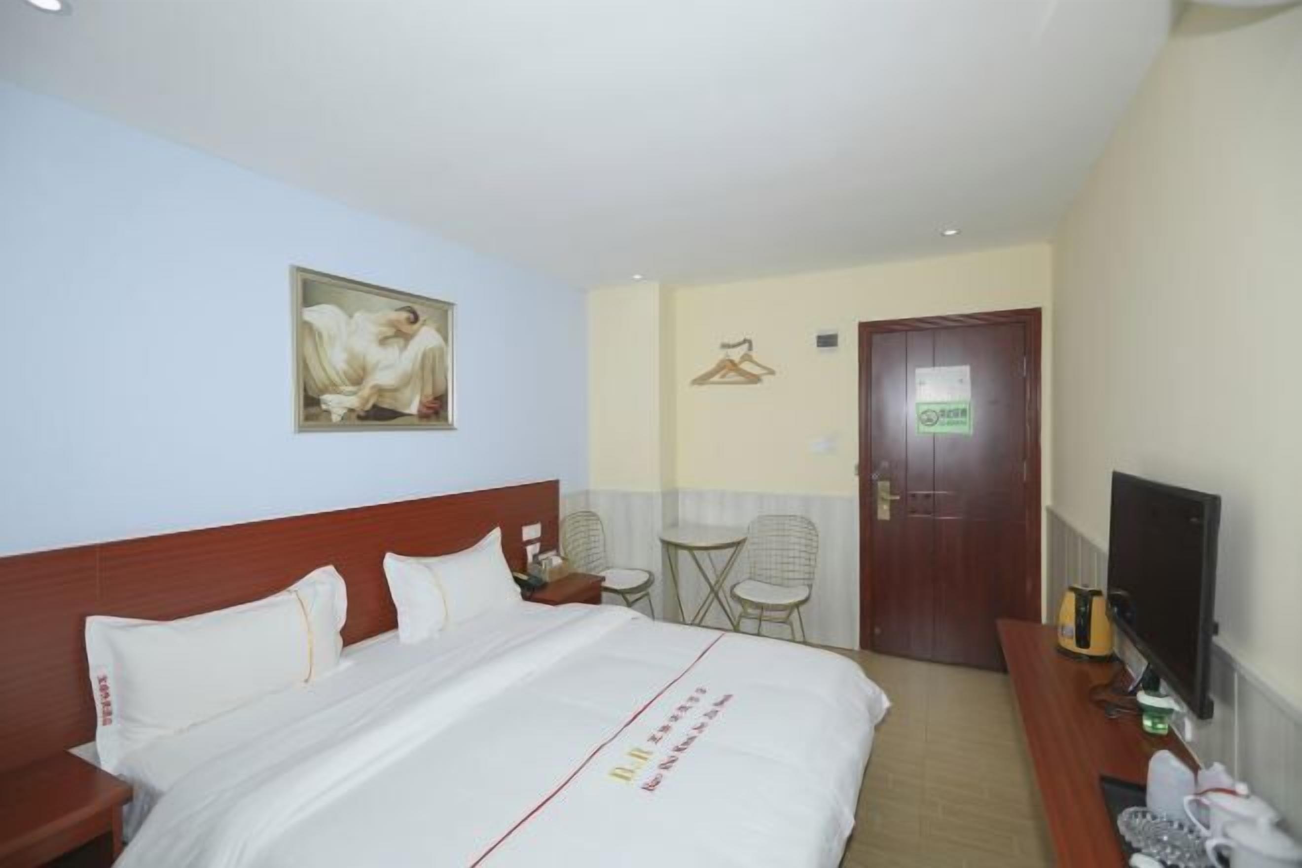 A hotel room with a bed, a television, a desk, and a door.