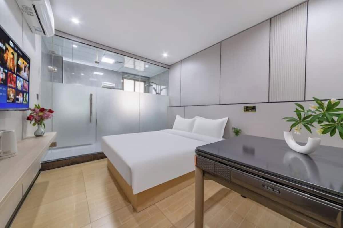 A modern hotel room with a bed, a desk, a TV, and a shower area.